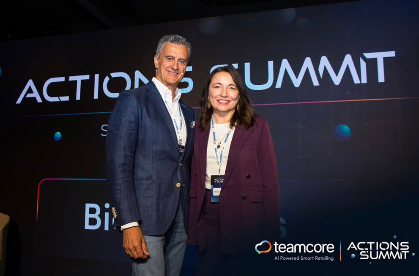 Two smiling professionals pose together in front of a dark backdrop that reads ACTIONS SUMMIT with Teamcore and summit logos visible.
